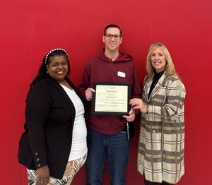 Two women and a man in the middle, holding a certificate; red background