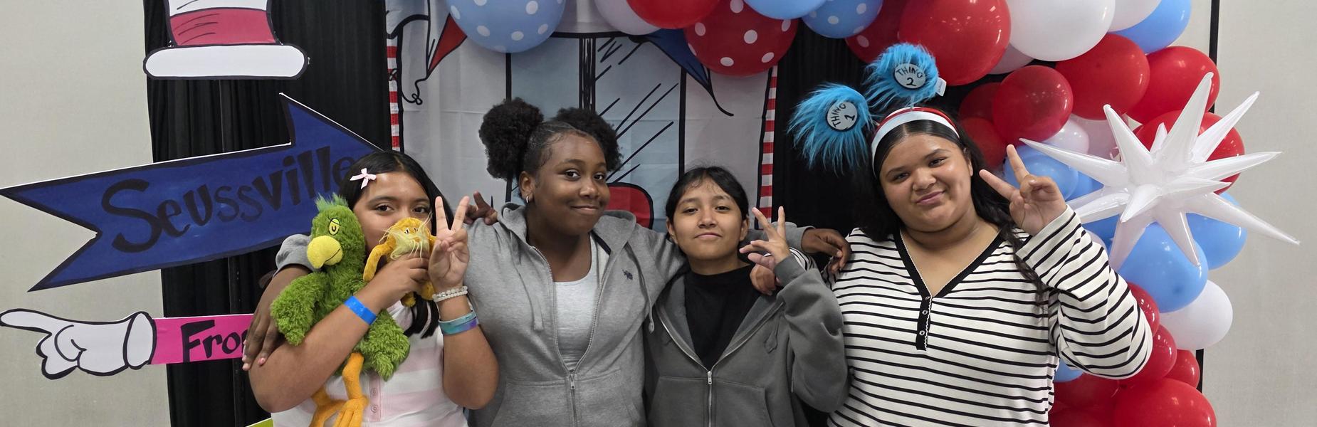 Four girls posing with stuffed toys in front of a decorated backdrop.