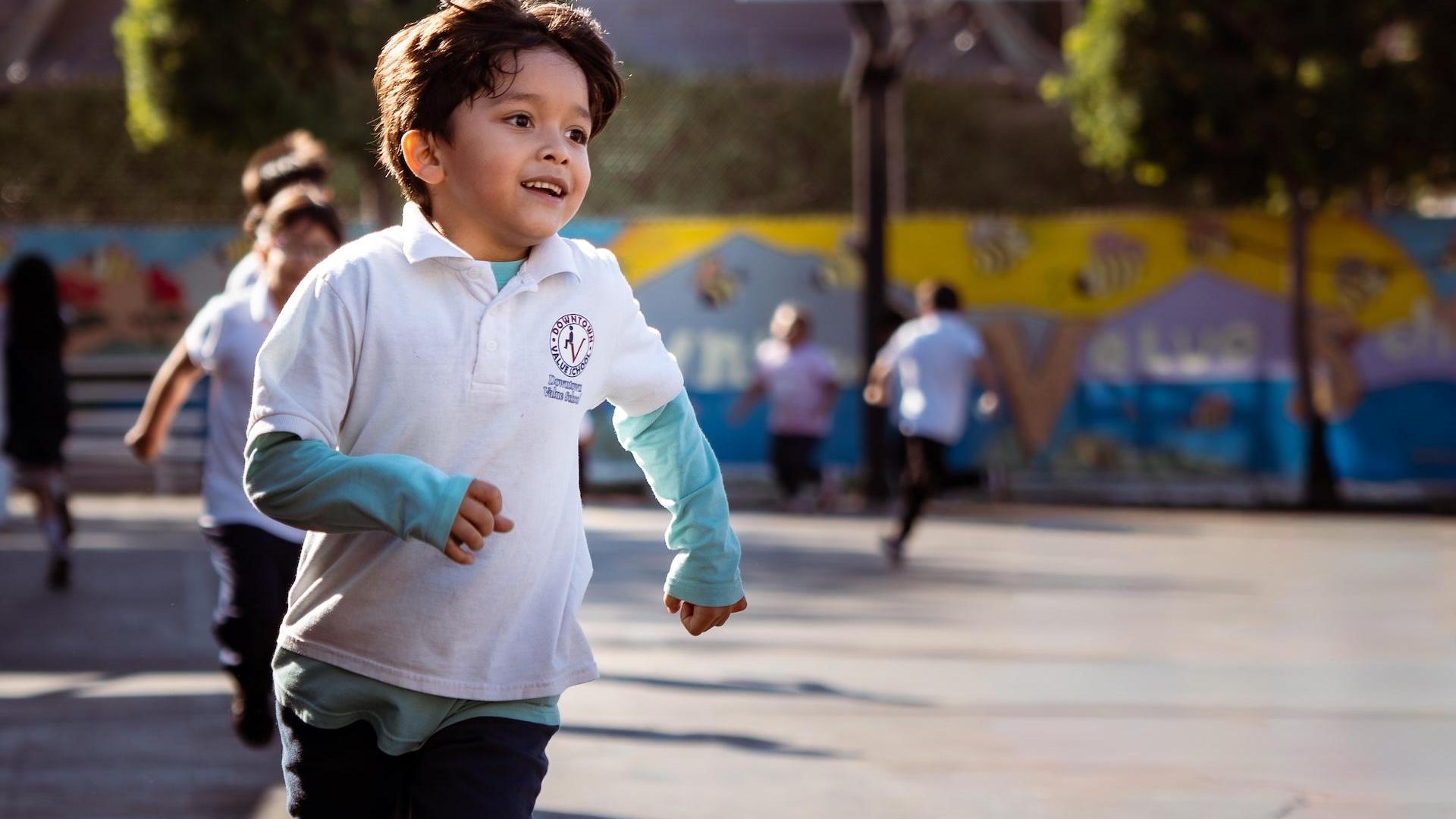 A young boy running joyfully in a playground filled with children.