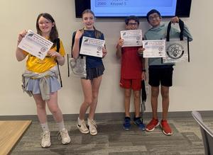 Four children displaying certificates and prizes, posing together.