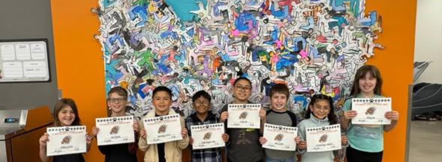 Children holding certificates in front of a colorful wall mural.