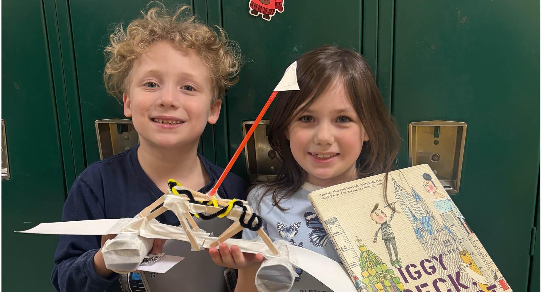 Two students are holding a book and a model bridge that they build together