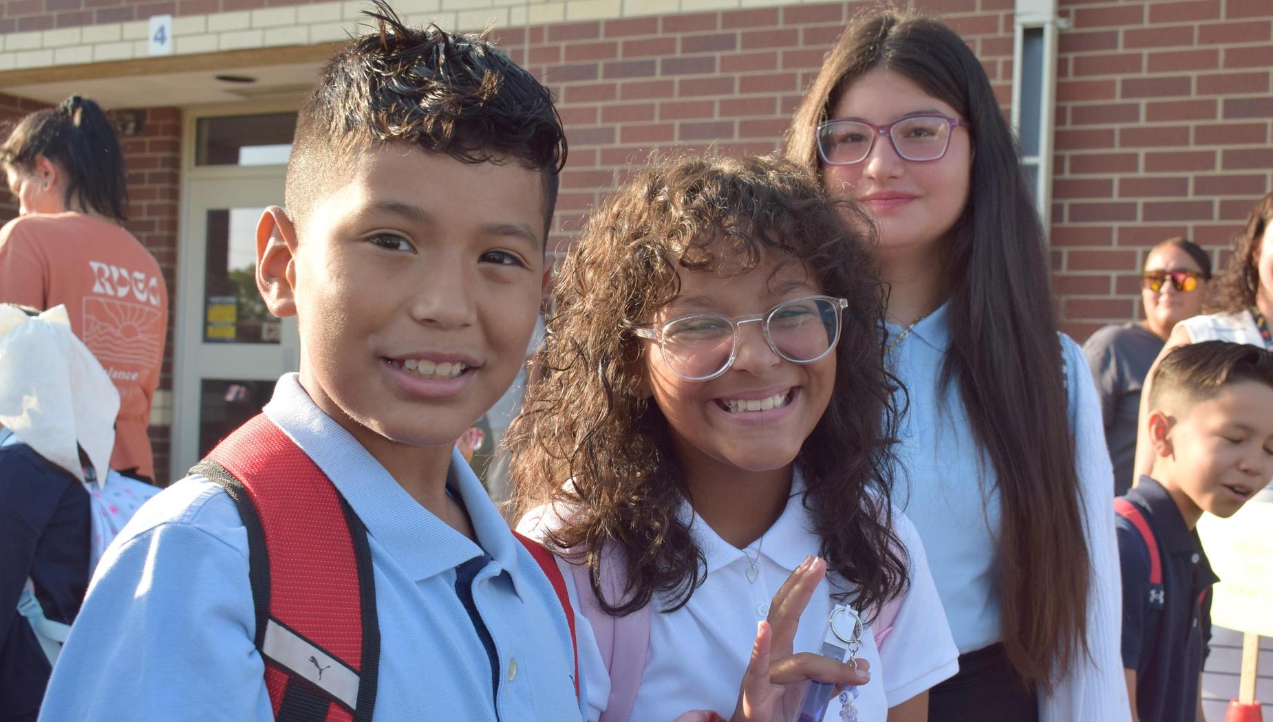 Three children smiling, one making a peace sign outside.