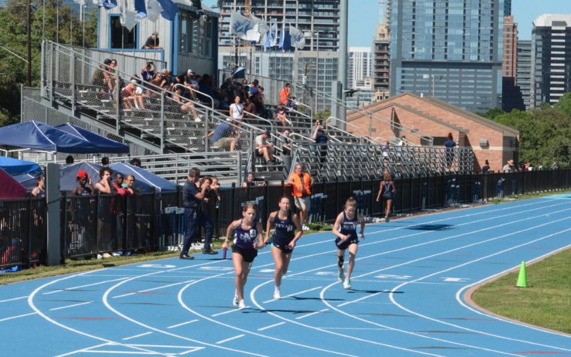 Three female athletes sprint on a blue outdoor track