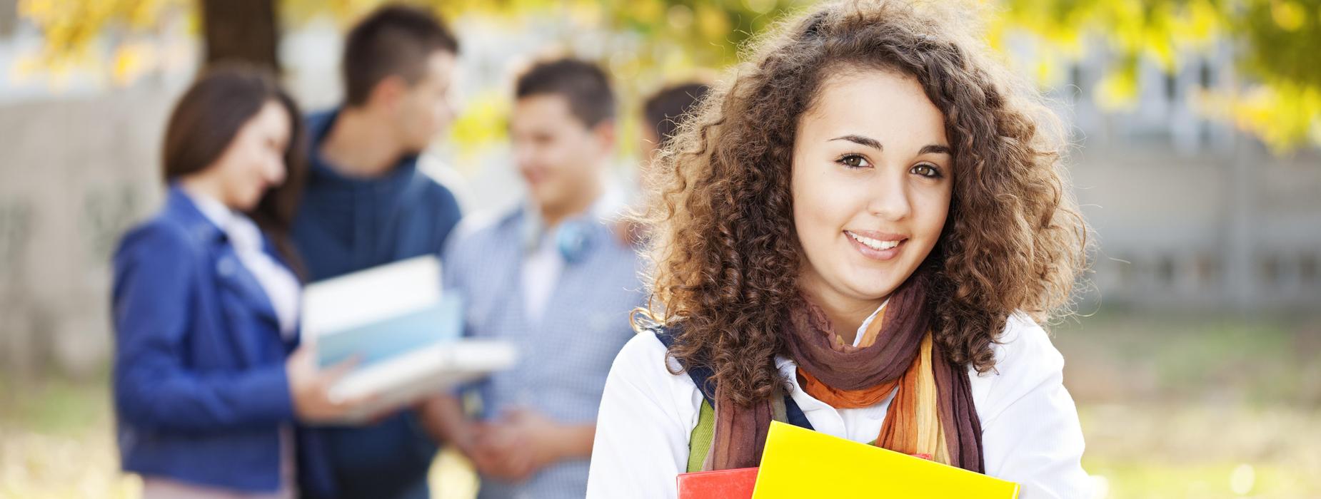 High school girl smiling.  Blurred image of 3 high school students in background