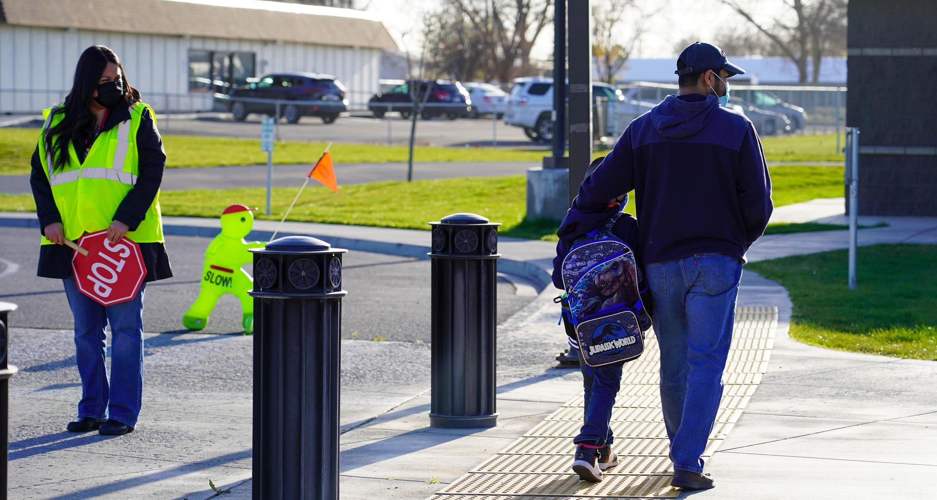 Cross guard is looking at a parent that is walking with his child.