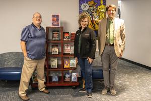 Julie Berry flanked by Jason Coleman and Kevin McGuire in front of a book stand
