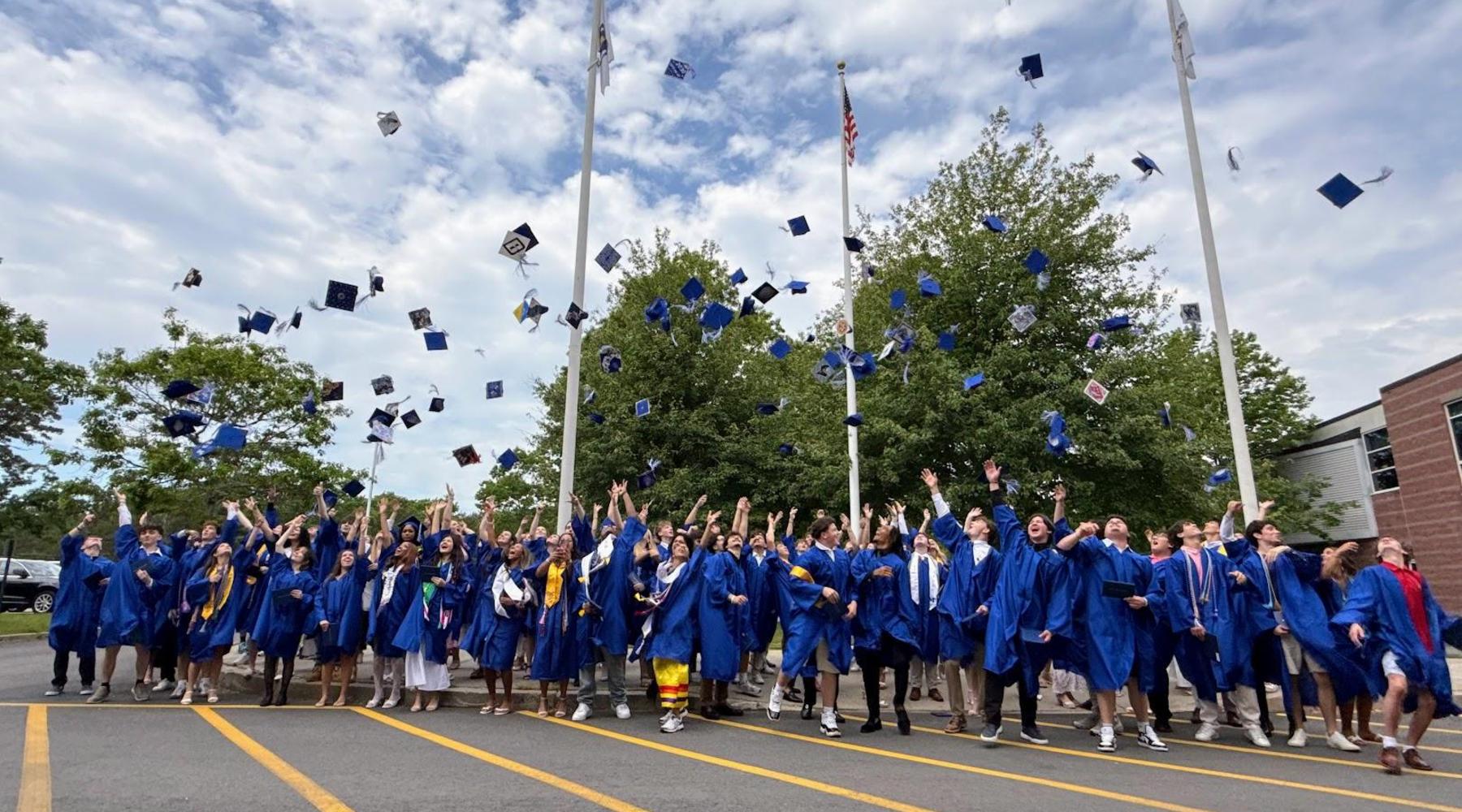 Graduates in blue gowns celebrating by throwing caps in the air outdoors.