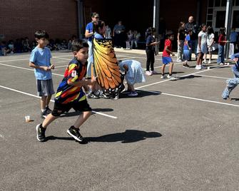 Kids playing in a school yard, one boy wearing a butterfly costume.