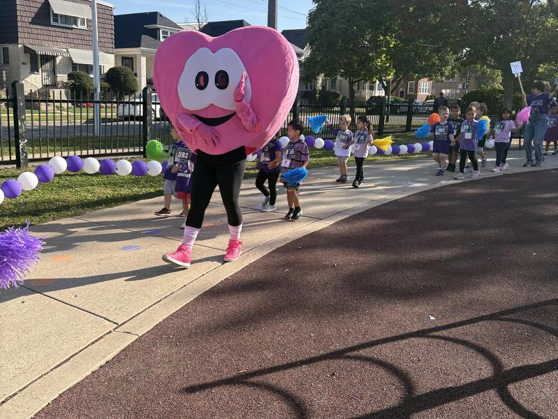 A person in a large heart costume leads children in a fun-run event.