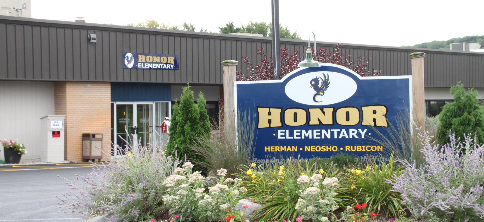 Sign for Honor Elementary School with building and flowers in foreground.