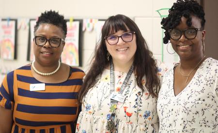 Three women posing together, smiling, in a bright, colorful setting.
