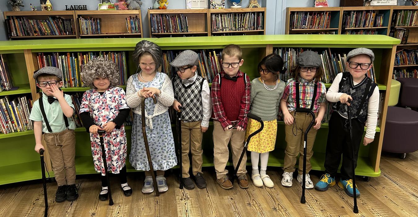 Group of children dressed as elderly characters with props in a library.