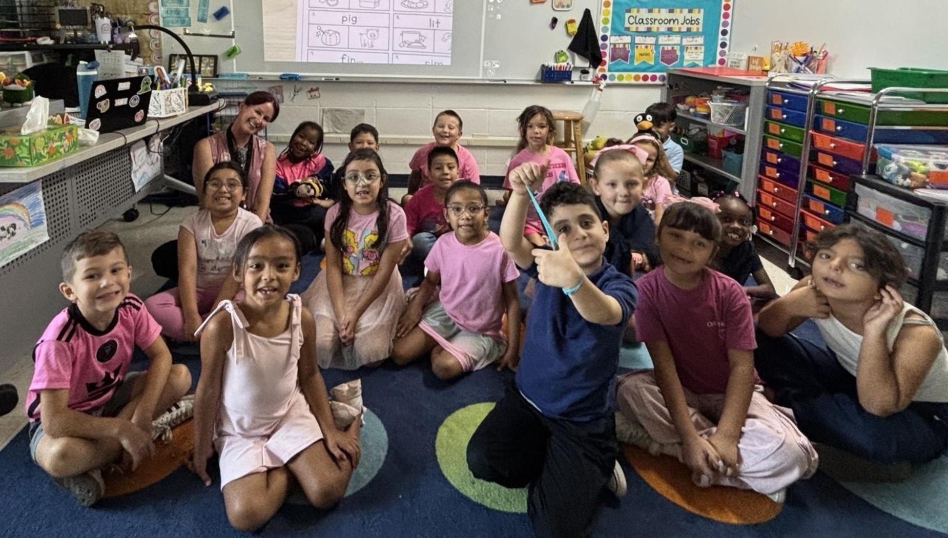 A diverse group of children and adults smile together in a classroom setting.