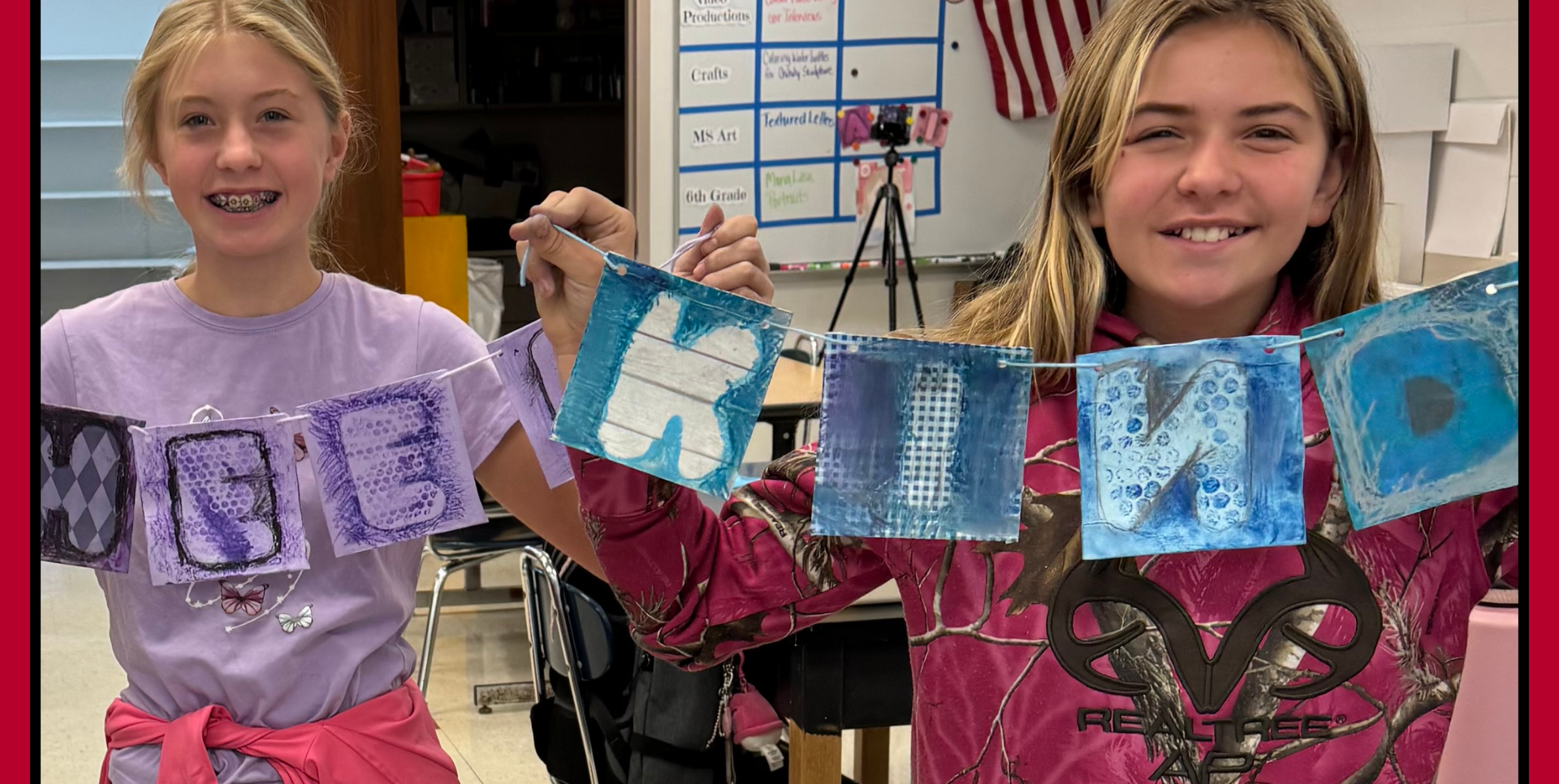 Two girls holding a banner with letters spelling 'BE KIND' in colorful designs.