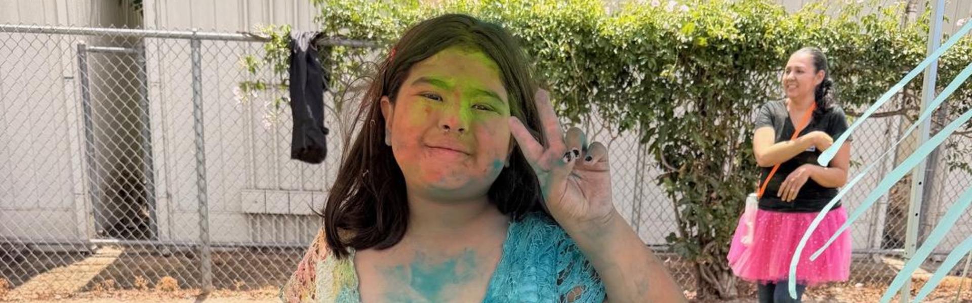 A girl with colorful powder on her dress, standing and smiling at the camera.