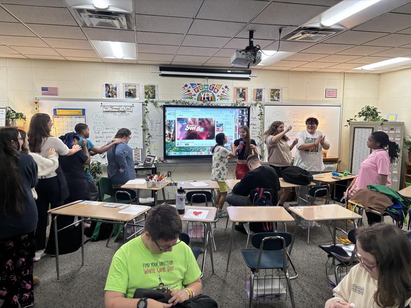 Students dancing in a lively classroom with an interactive screen.