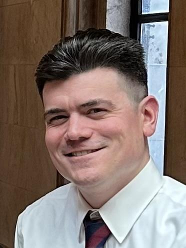 Smiling man in a white shirt and tie posing in a well-lit indoor setting.