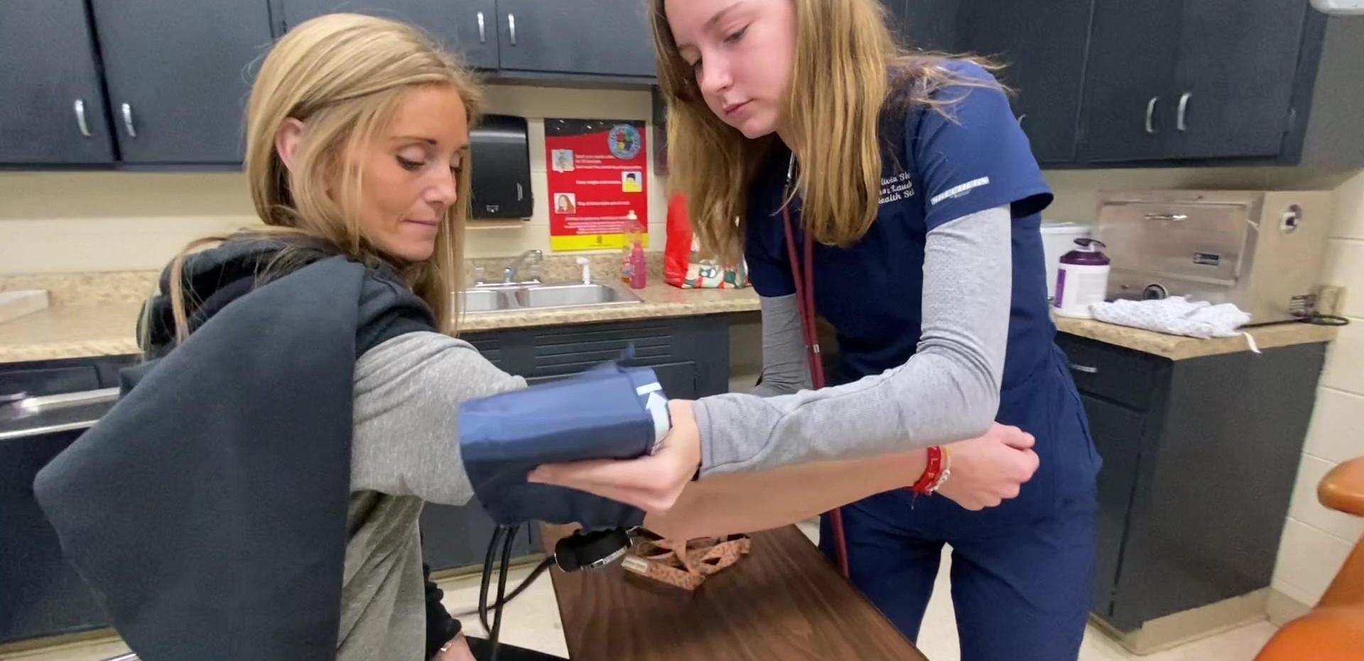 Nurse taking a woman's blood pressure in a medical setting.
