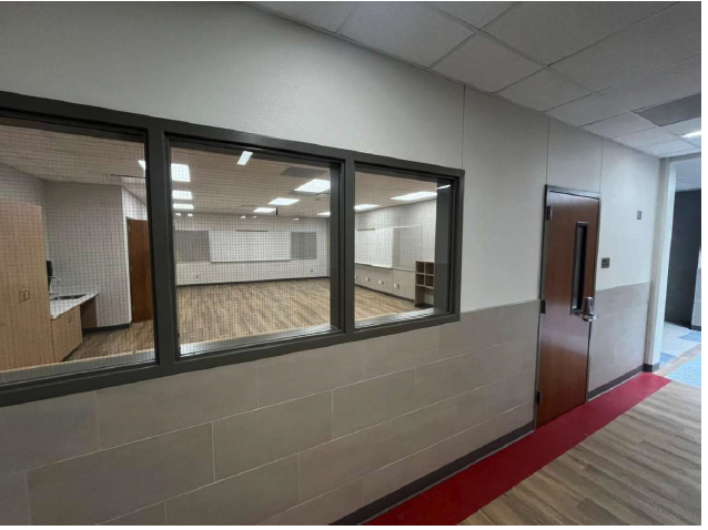 Hallway with large windows leading to an empty, bright classroom.