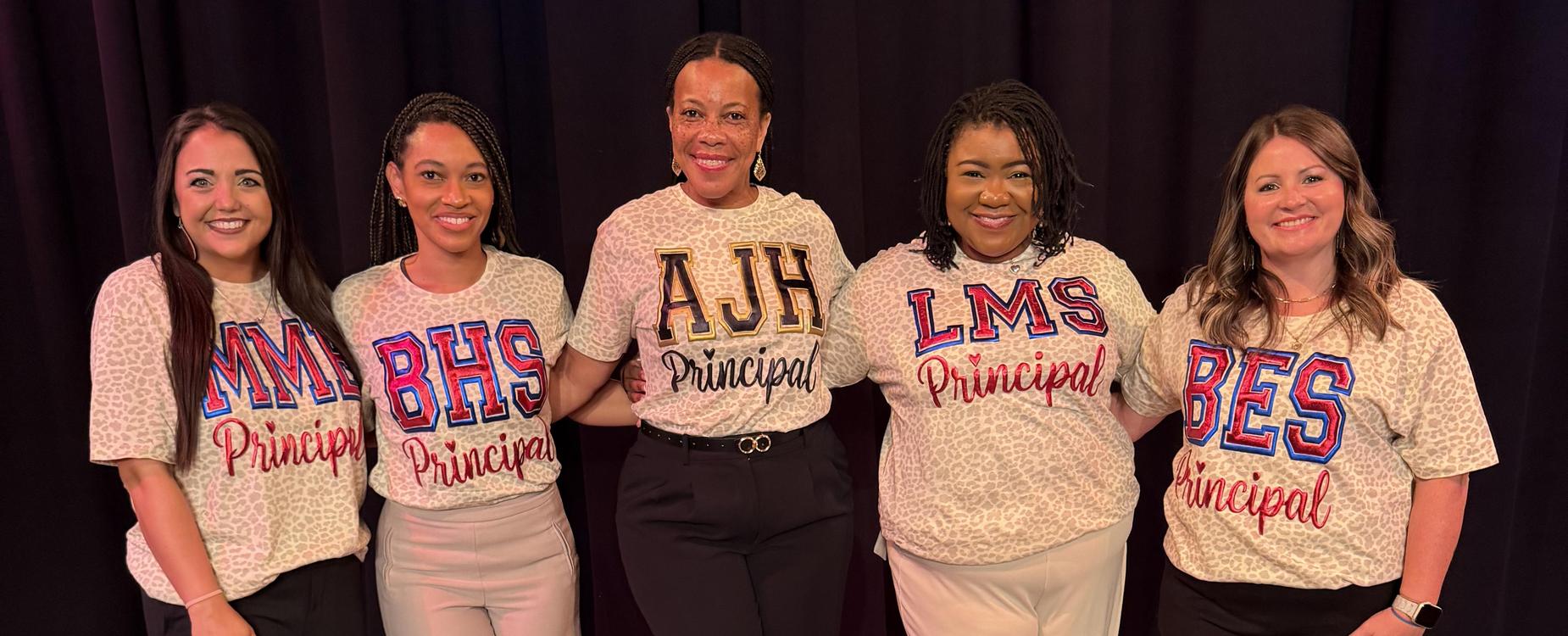Five women in matching shirts with school initials and the word 'Principal'.