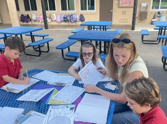 3rd grade teacher working outsdie with 3 students on narrative story