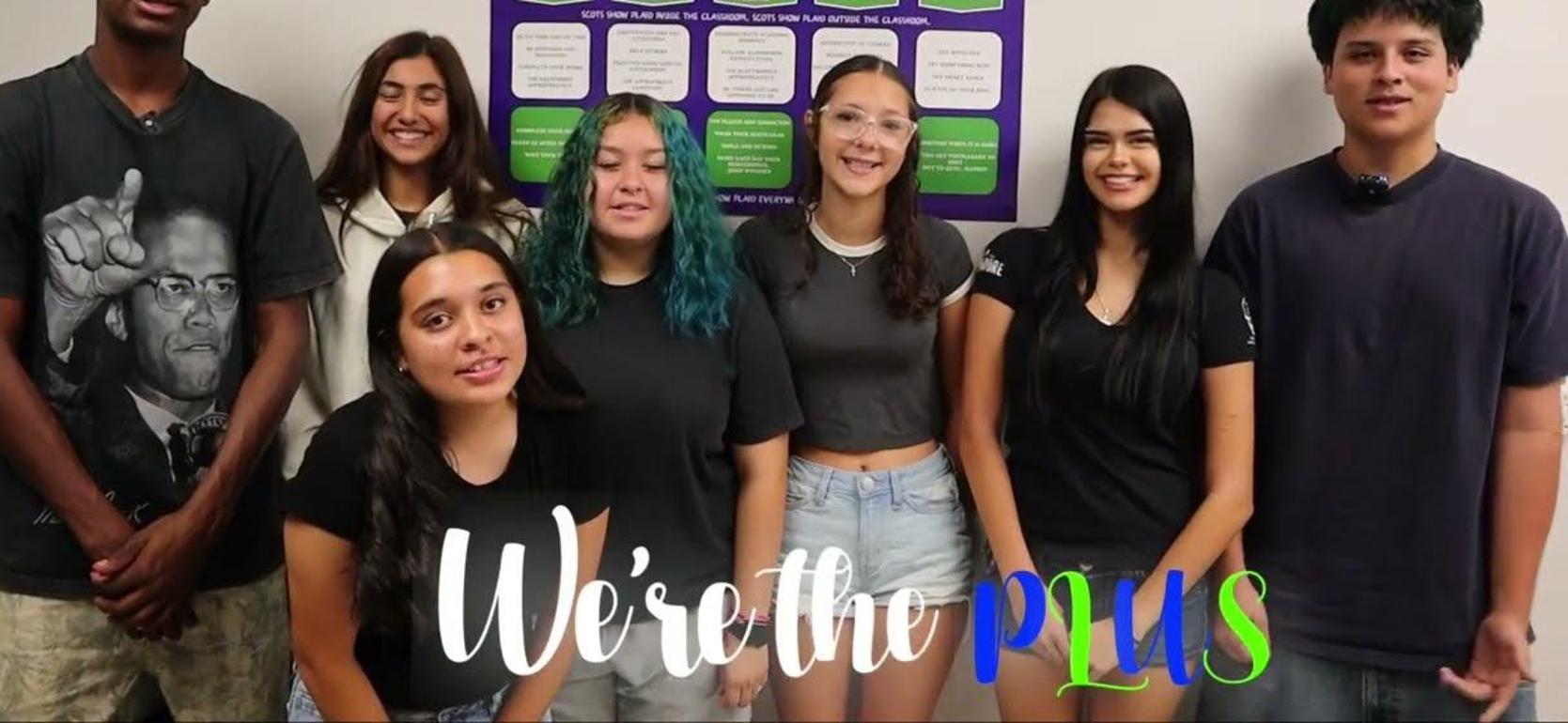 Group of students posing together in a classroom with a poster in the background.