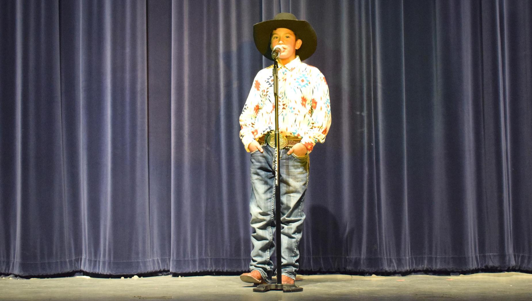 A young boy performing on stage in cowboy attire.