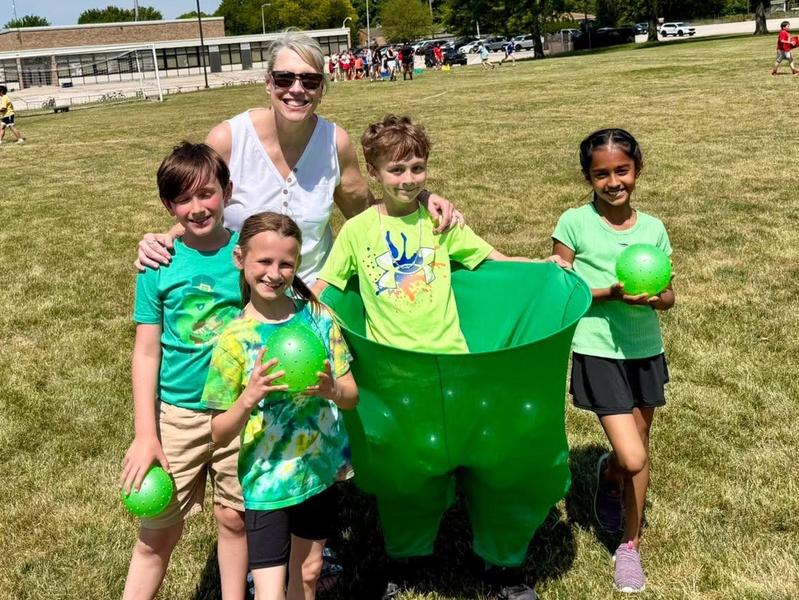 Group of children holding green balls with an adult in a grassy outdoor setting.