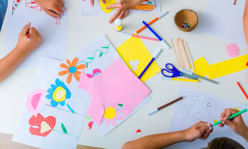 Overhead view of a table with children's art supplies and hands working on projects