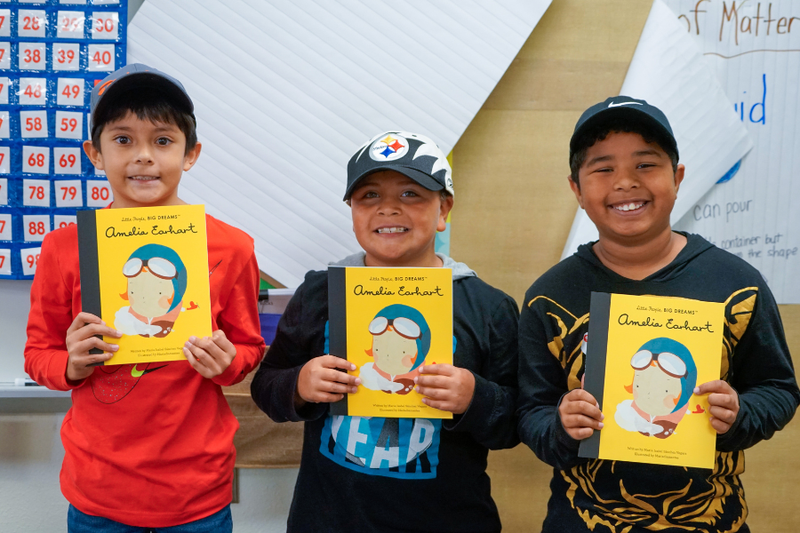 Three students holding the same book from United We Read event.