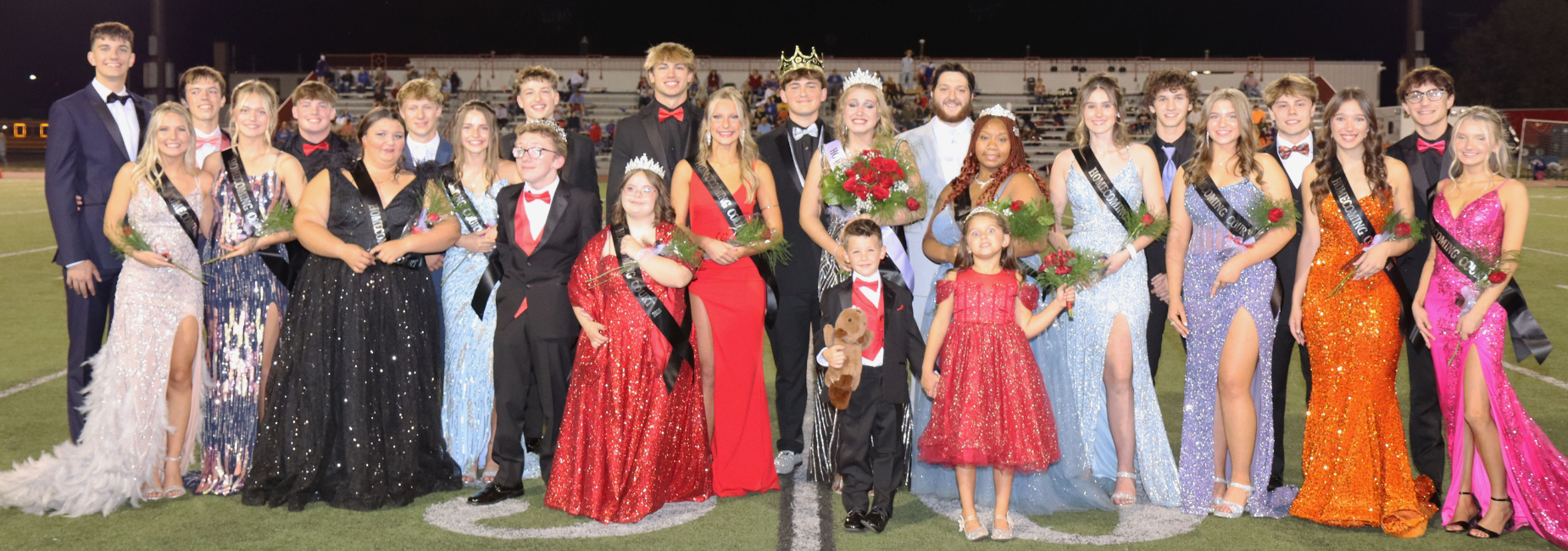 A large group of students in formal wear posing together on a football field.