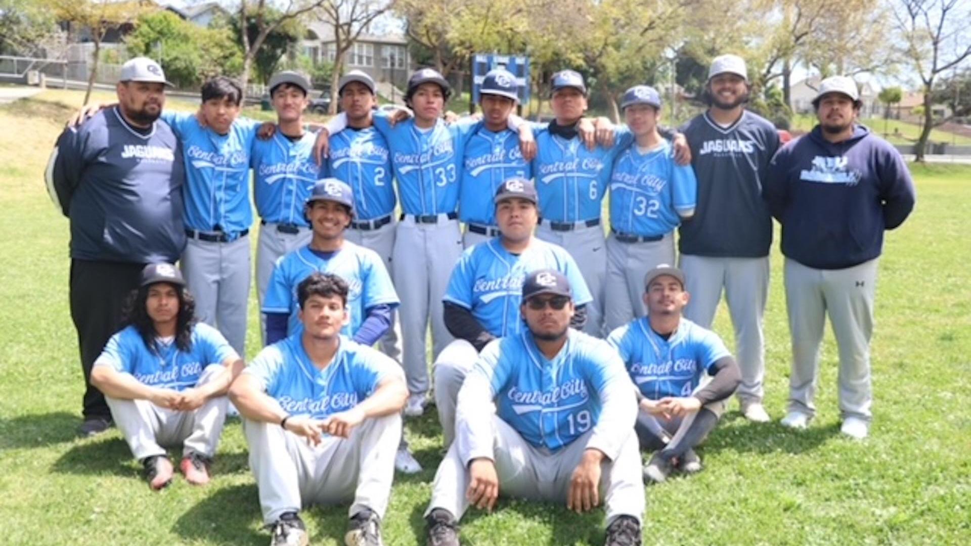 A youth baseball team in blue uniforms poses on a field, with coaches and players arranged in two rows.