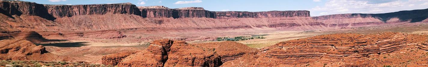 Hikers traverse a rocky, red landscape with distant mesas under a blue sky.