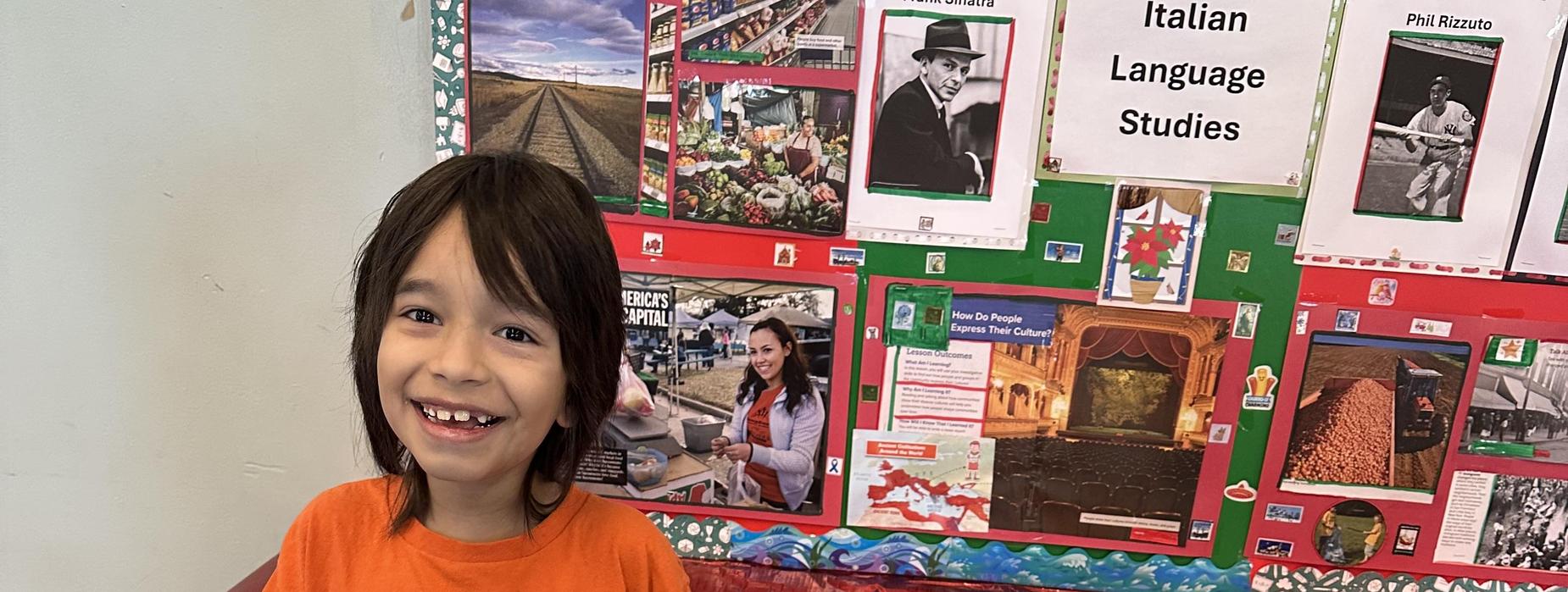 Child in an orange shirt smiling in front of a decorated table.