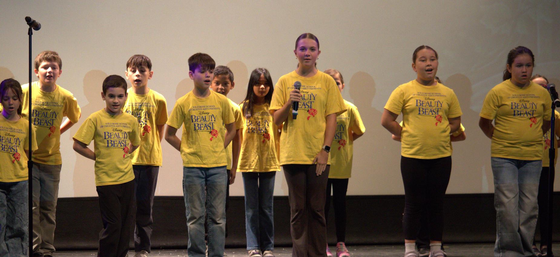 A children's choir performing on stage, all wearing yellow t-shirts.