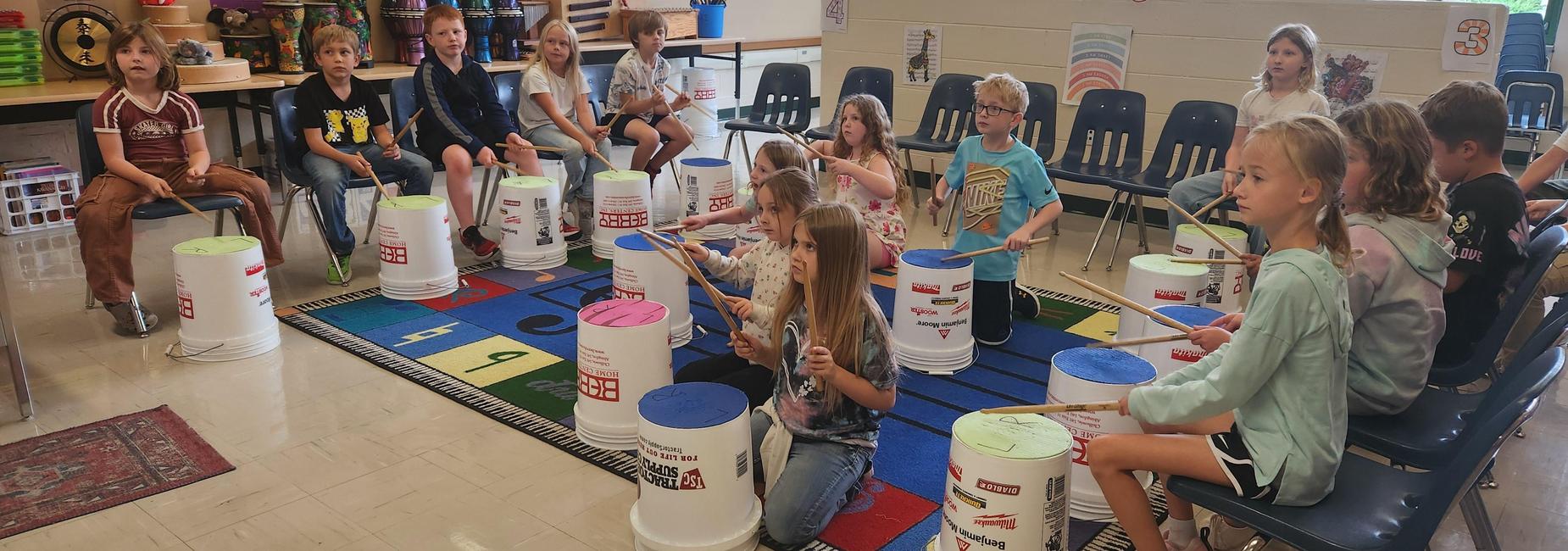students playing 5 gallon bucket drums during music class