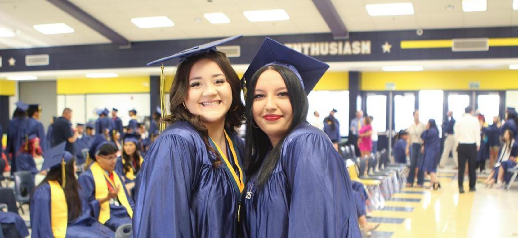 Two graduates posing together, both in caps and gowns, smiling at the camera.