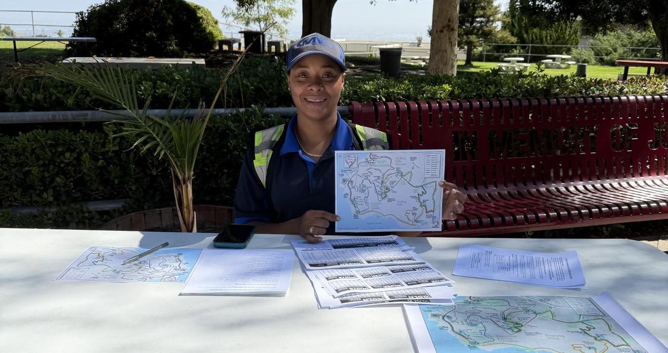 A woman in a cap shows a map and papers at a table outdoors.