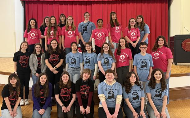 Students posed on a stage in matching t-shirts.