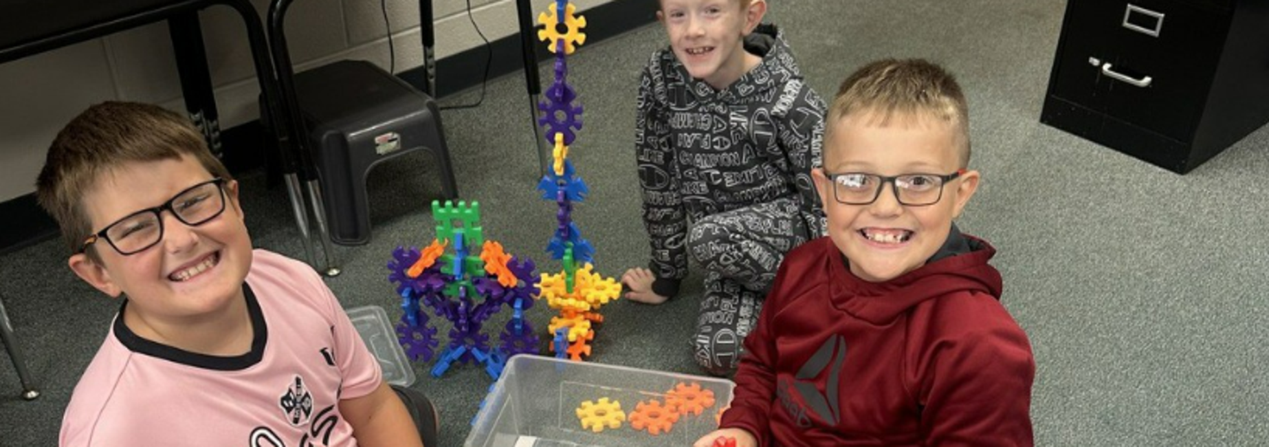Two boys playing with colorful building pieces on the floor, smiling at the camera.