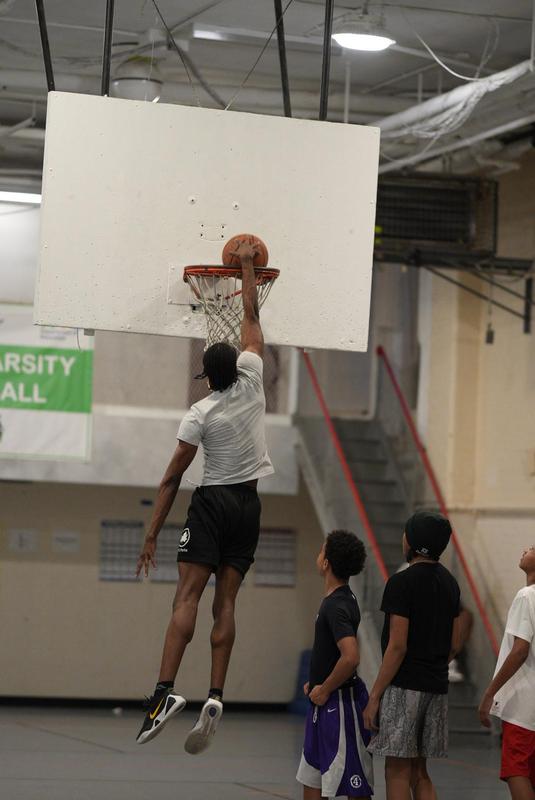 A player dunks a basketball while teammates watch in a gym.