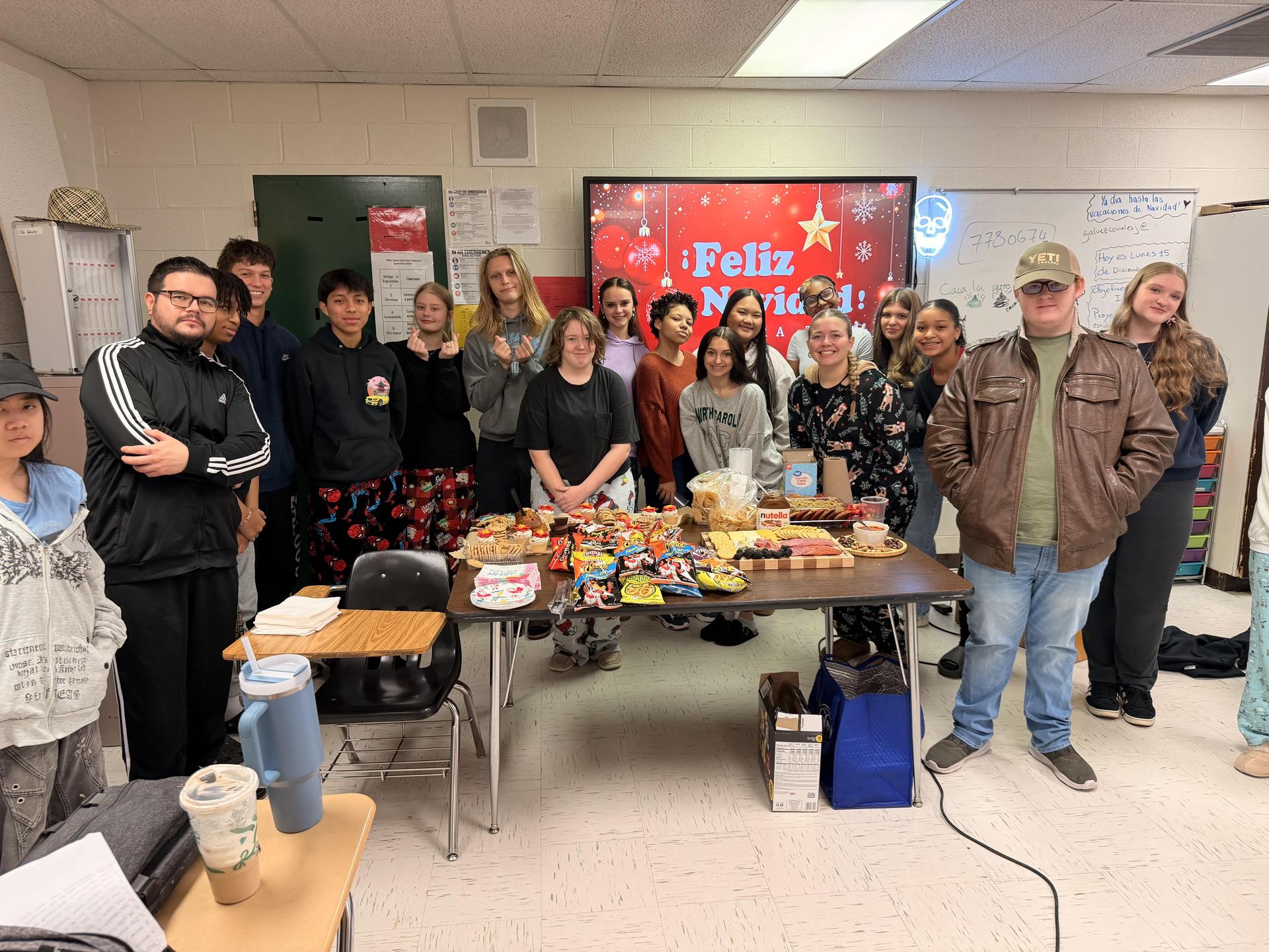 A class gathering around a table filled with snacks, celebrating together.