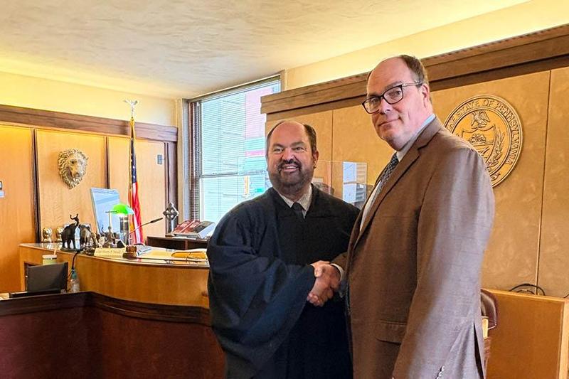 Judge Smail and Dr. Harris stand in the courtroom and shake hands