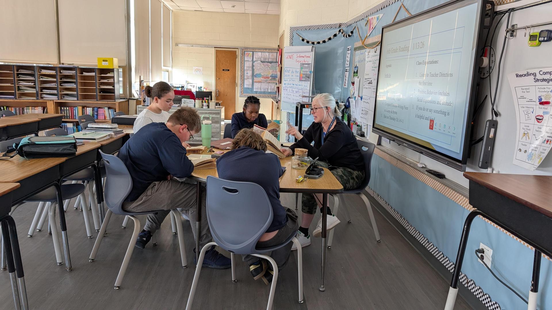 Teacher working with students at a small desk. 