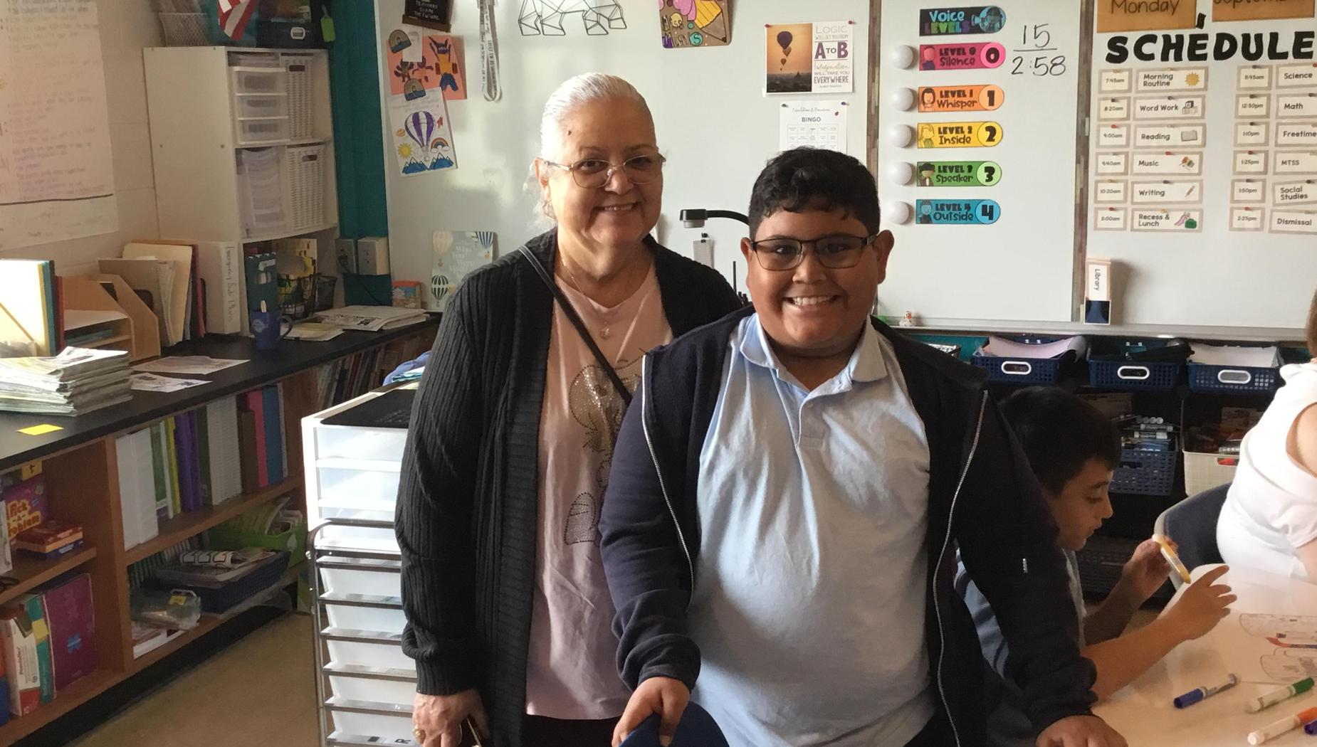 A child and an older woman standing together in a classroom setting.