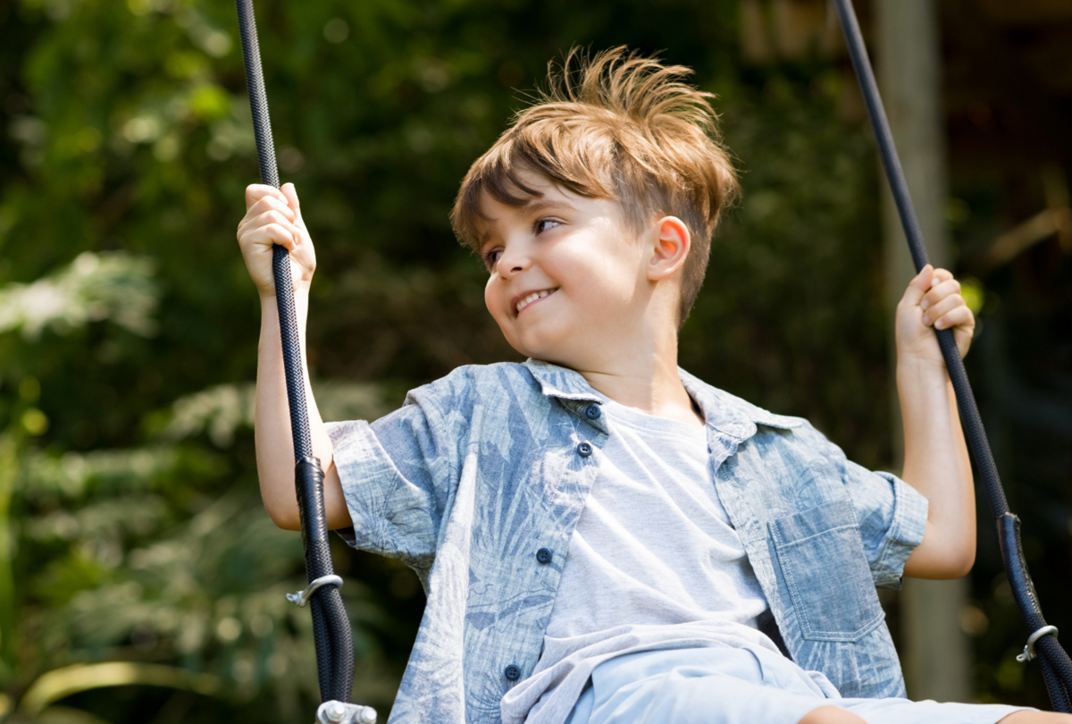 boy in jean shirt swinging in summer