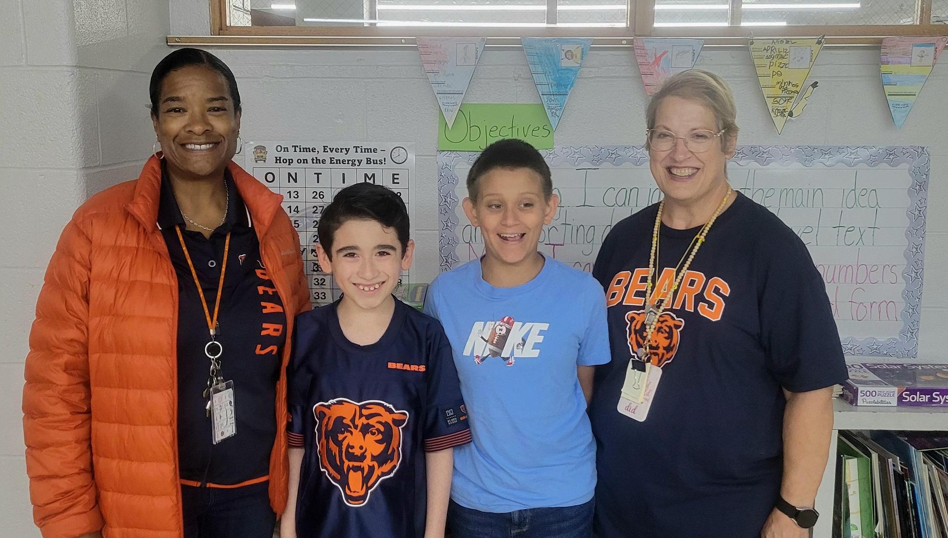 Four people, two adults and two children, smiling in a classroom setting.