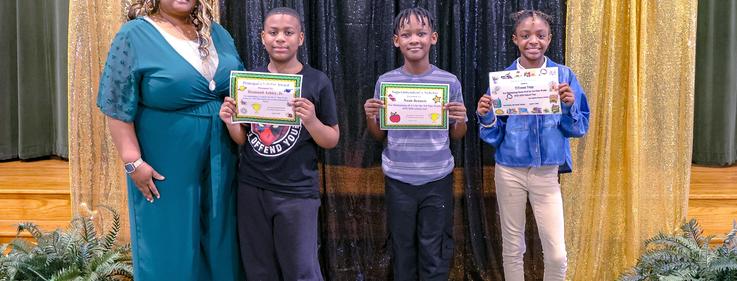Four people standing together, holding certificates at a ceremony.
