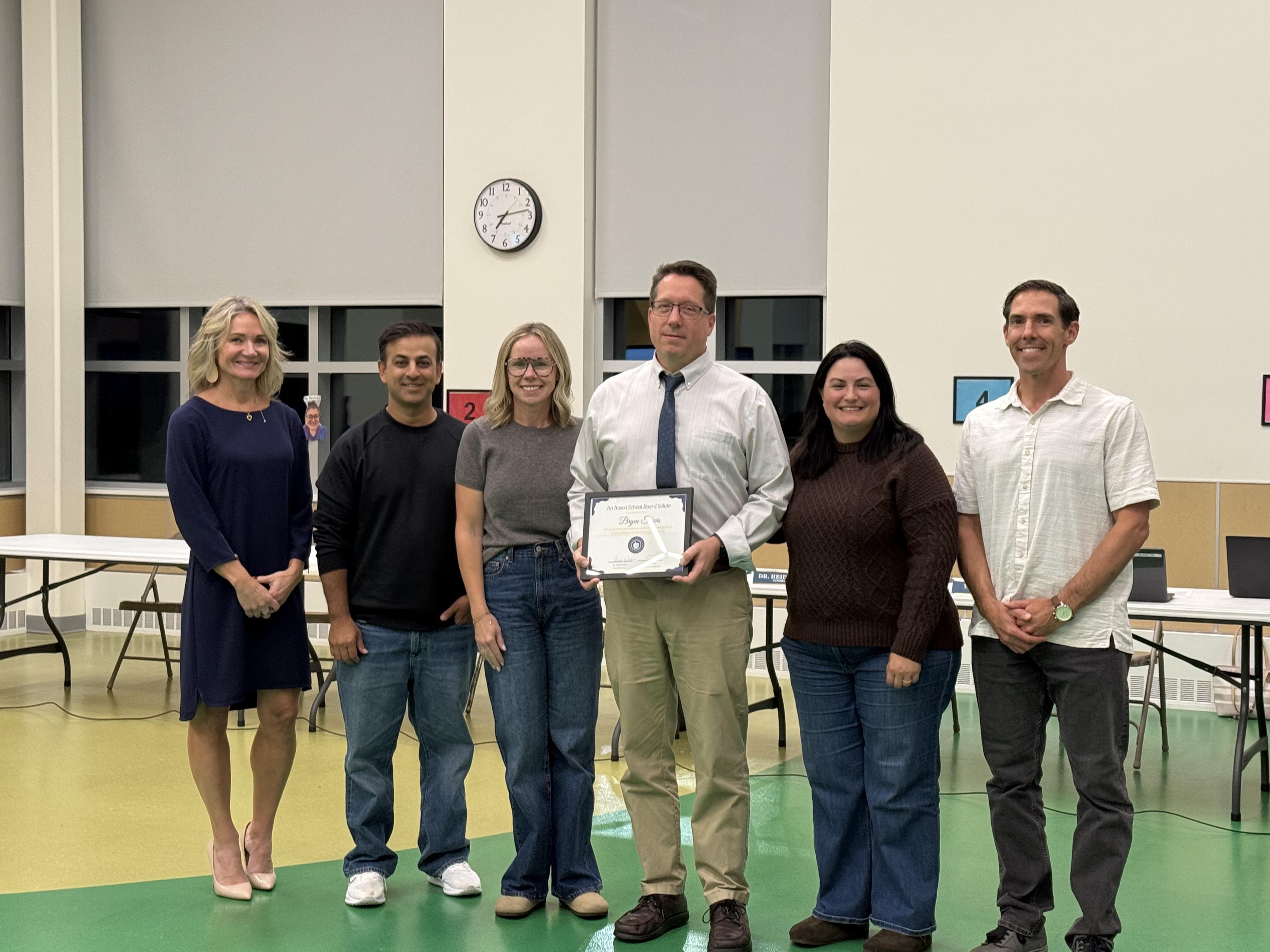 Group smiling at a board meeting with a teacher holding an award